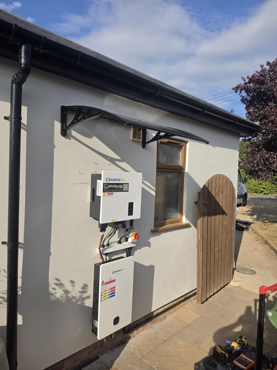 Inverter and battery on a rendered wall under a canopy