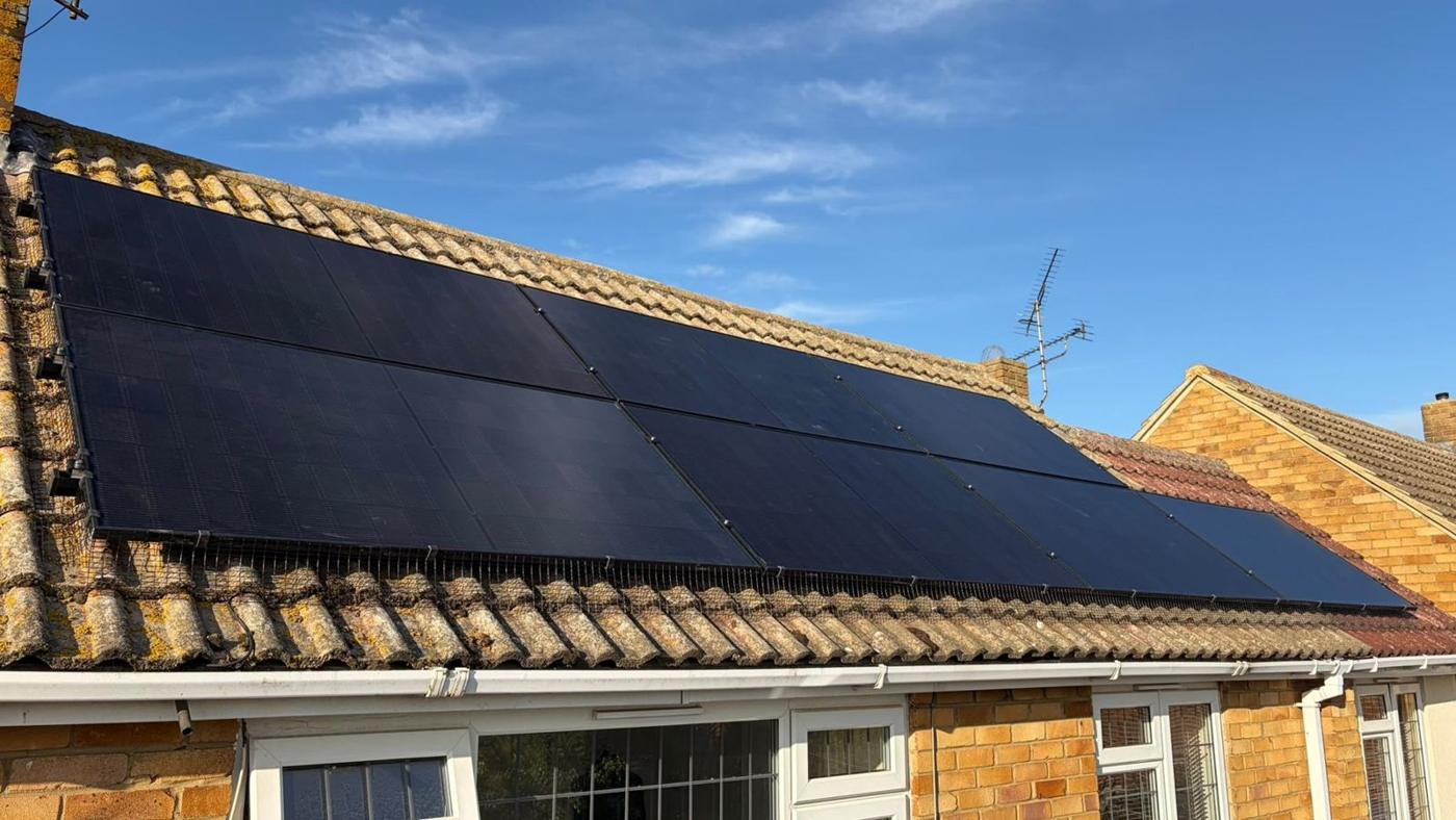 All-black solar panels on a bungalow roof under a blue sky
