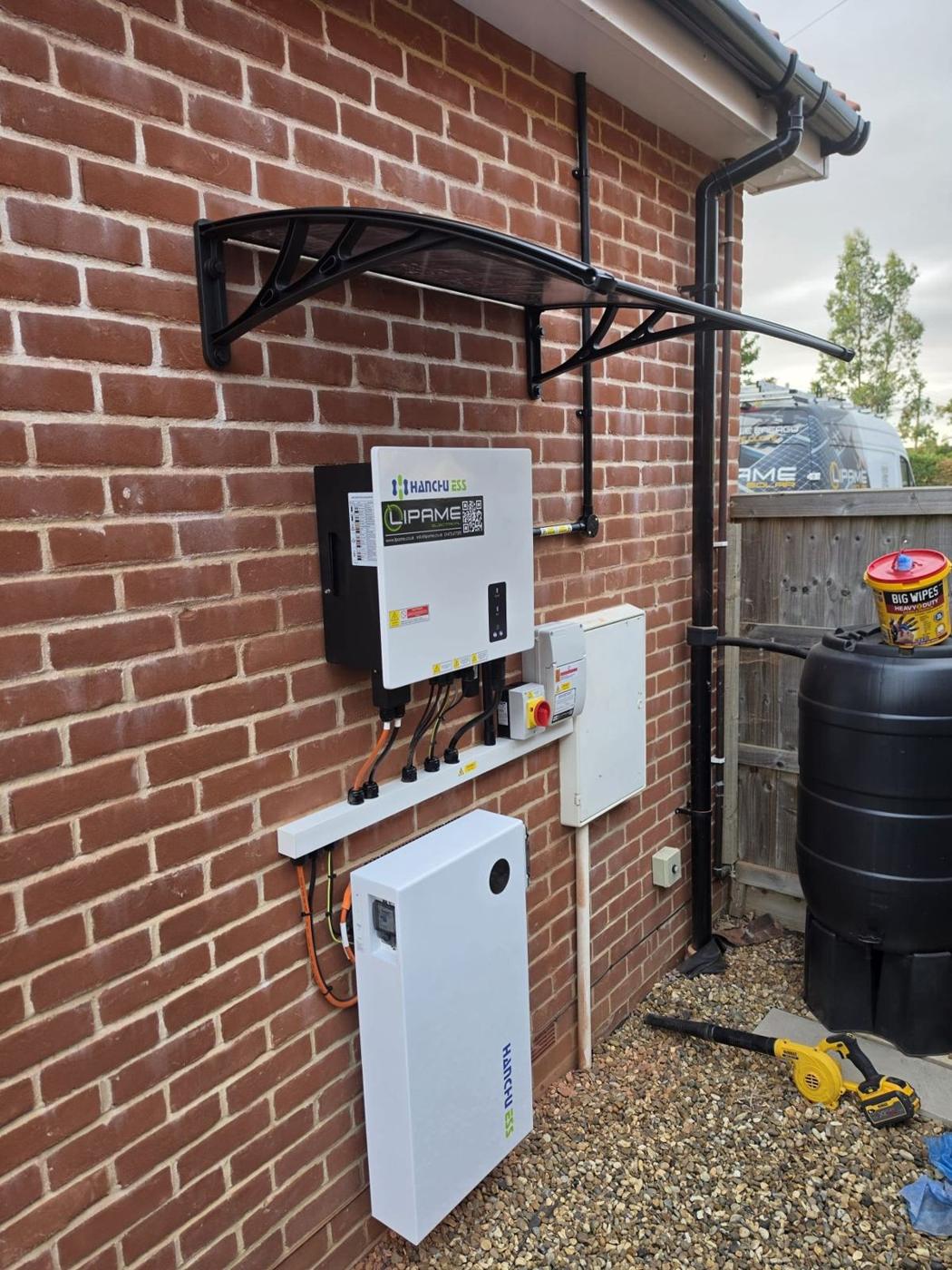 Hybrid inverter and home battery on a brick wall under a black canopy